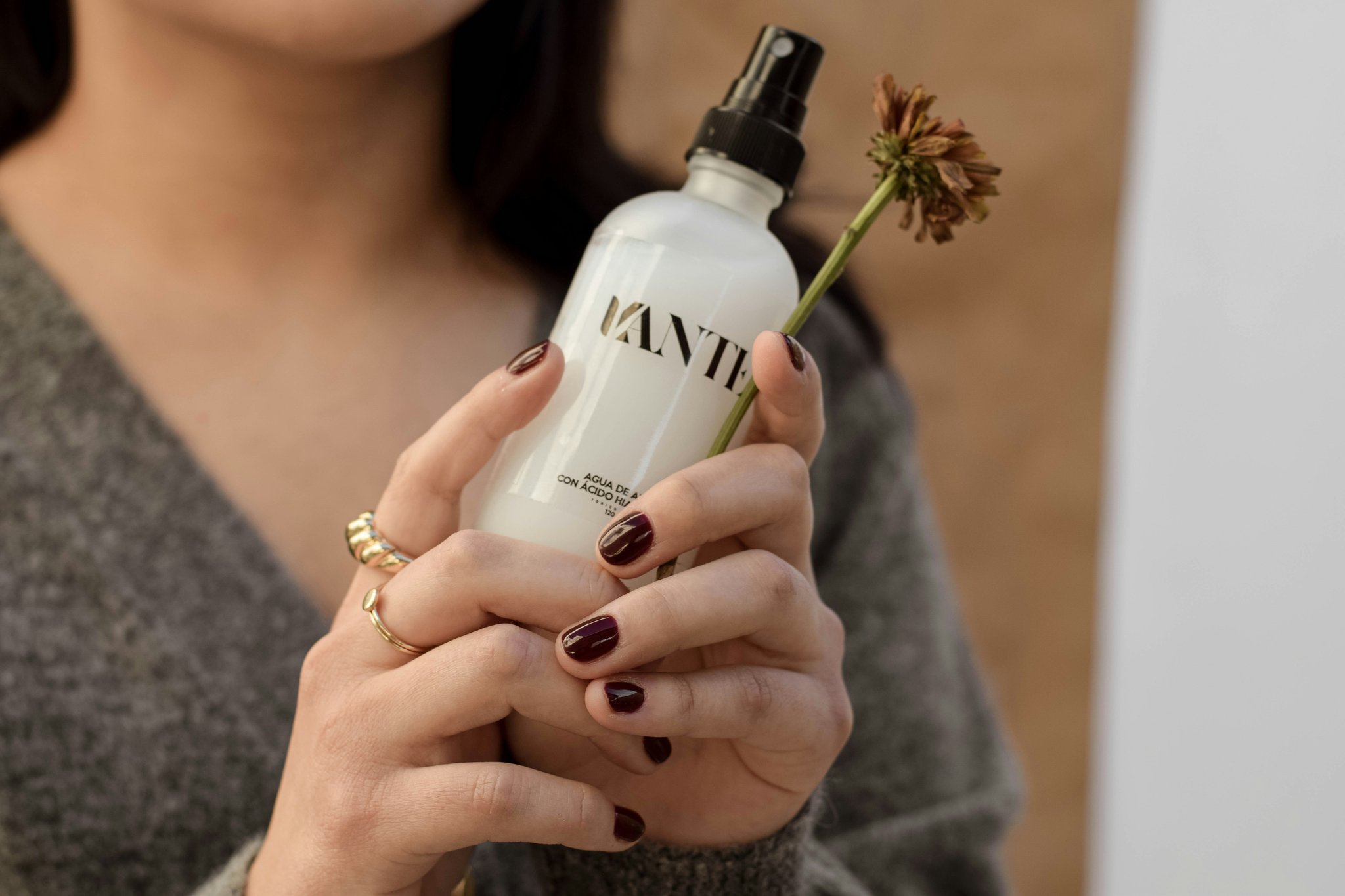 A smiling woman holding a bottle of vegan serum with glowing skin